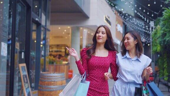 亚美两名女子在百货公司户外购物年轻漂亮的女性朋友拿着购物袋一起在购物中心快乐地购物
