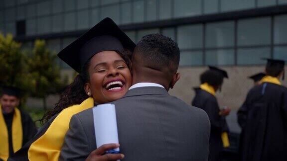 毕业典礼当天一名快乐的非裔美国研究生抱着父亲手里拿着毕业证