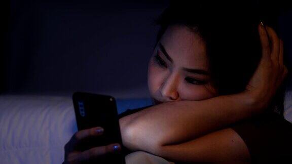 沮丧的年轻美丽的亚洲女人独自坐在卧室地板上使用智能手机不快乐的压力少女坐在地板上看手机带着负面情绪