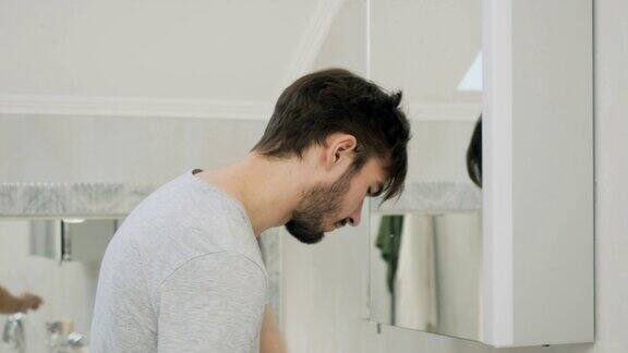 一个昏昏欲睡的年轻人在镜子前用牙刷刷牙