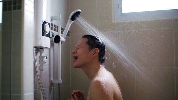 年轻的亚洲男人在浴室里用慢动作洗淋浴