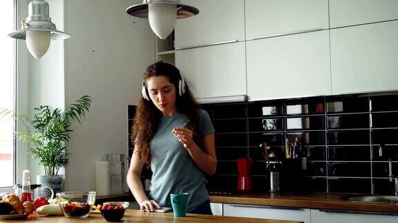 迷人的快乐女孩早上在厨房边跳舞边唱歌边使用智能手机在家里听音乐