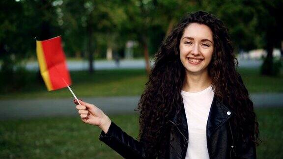 慢动作肖像迷人的女孩世界旅行者挥舞比利时国旗看着相机和微笑站在绿色公园在夏天人与旅游理念