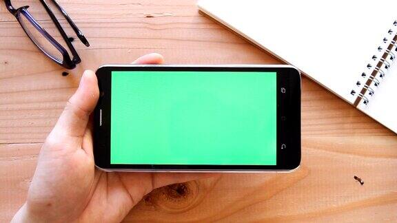 手用手机与绿色屏幕上的木制办公桌顶视图