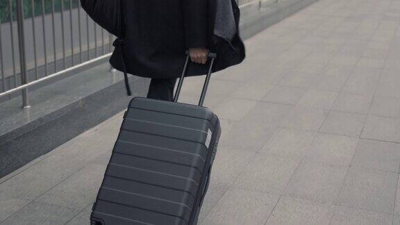 一个穿着黑色外套带着黑色行李箱的男人走在机场候机楼的后面
