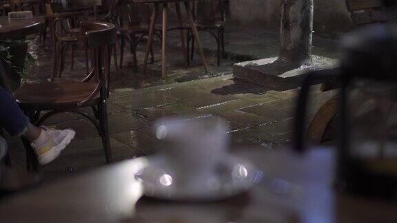 雨中夜晚的户外街头咖啡馆坐在桌子旁的人面目全非雨点落在人行道上欧洲老城区街头露天咖啡馆下起了倾盆大雨