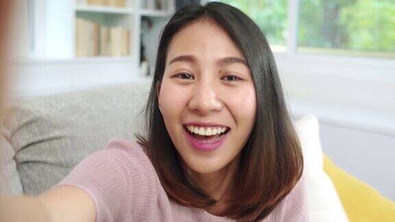 年轻的亚洲少女在家里做视频博客女性在客厅用智能手机制作视频到社交媒体生活方式女人在家里放松上午