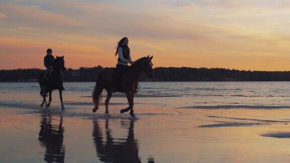 夕阳下的海滩上骑马的两个人