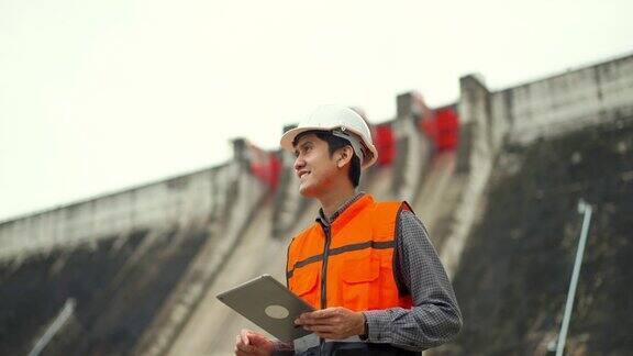 自信的亚洲维修工程师在工地用平板检查水电站大坝和灌溉在大型建筑工程中戴安全帽的工程师