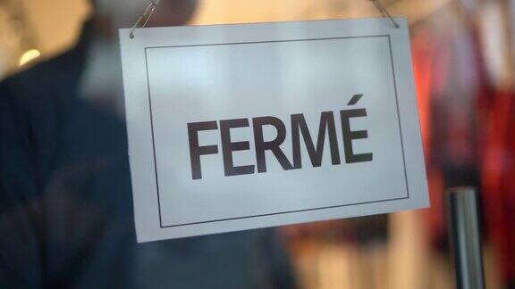 店主转向关门的标志(fermé)在店面门口