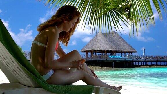 年轻女子美丽的腿使用防晒霜在热带海滩上缓慢的运动
