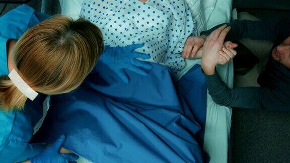 在医院里妇女在分娩产科医生协助丈夫握着她的手支持配备专业助产士的现代产科病房自上而下俯瞰