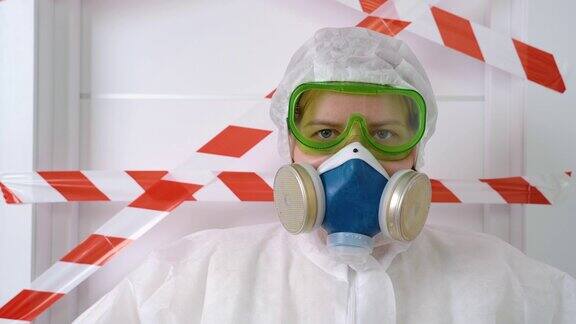 一名妇女穿着危险物质防护服带着自给式呼吸器和防护面罩在实验室里大口呼吸并四处张望门上有生物危害警告标志