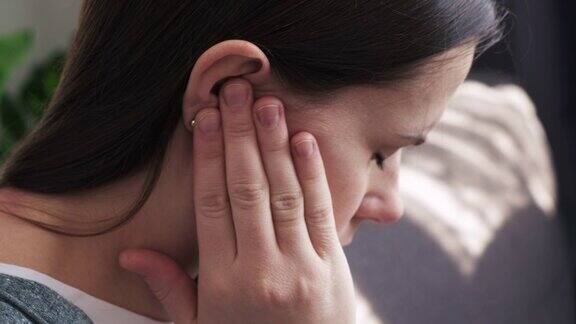 心烦意乱的年轻黑发女性抱着疼痛的耳朵突然感到强烈的疼痛不健康的白人妇女坐在家里的沙发上患有痛苦的中耳炎健康问题概念