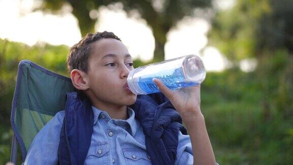 小男孩在野外露营时使用可重复使用的水瓶喝水