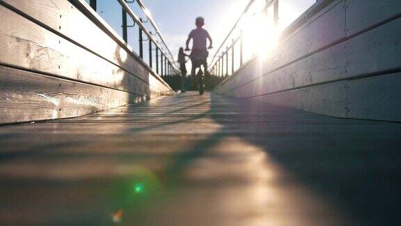 夕阳西下的木桥上一个小男孩骑着自行车经过一个小提琴手的身影