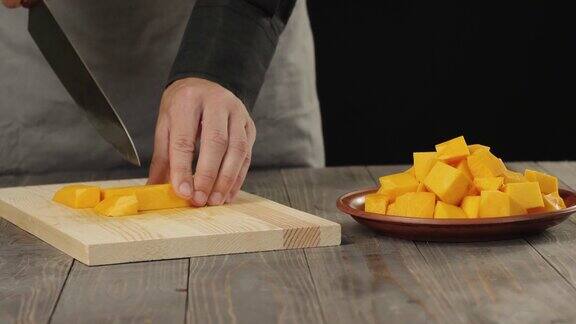 煮奶油南瓜汤健康食品厨师在木桌上把一个新鲜的橙色南瓜切成小块侧视图4k