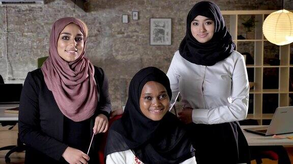 商业团队的三个年轻的穆斯林妇女戴着头巾看着镜头和微笑在现代办公室