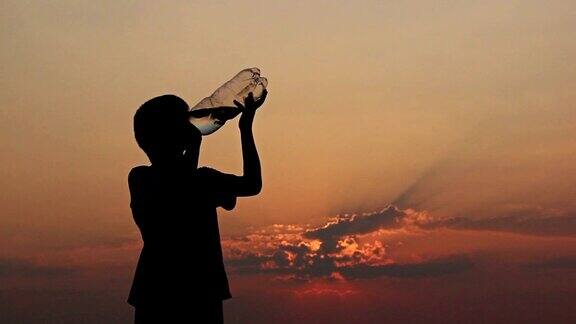 男孩在日落时喝瓶子里的水剪影少年