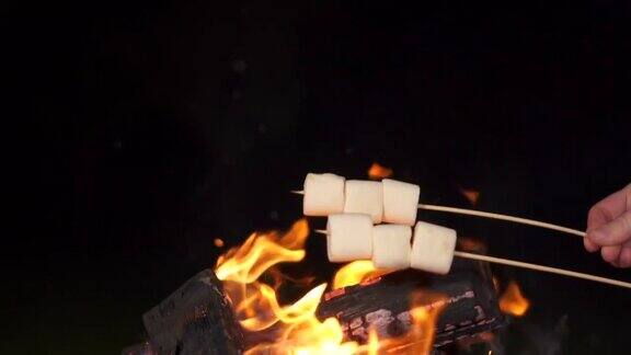 棉花糖棒烤篝火在黑色背景人们在壁炉旁烤棉花糖享受他们的假期朋友们在烤架上烤棉花糖的特写