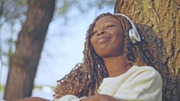 开朗的黑人女性戴着耳机在公园里用手机听着最喜欢的歌