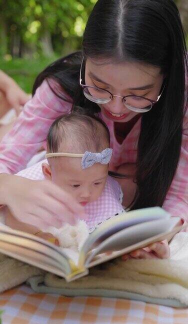 妈妈抱着书一起给小女孩看亚洲家庭带着一个孩子在野餐的时刻周末的活动中感受幸福的时刻积极的情绪