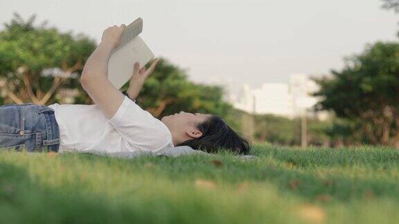 迷人的美丽年轻的亚洲女性轻松地阅读而躺在地板上的草