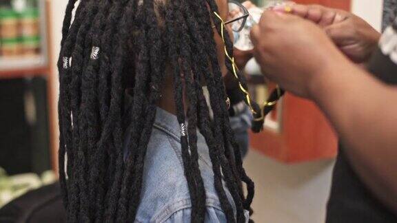 发型师在沙龙预约期间为客户的发辫编织金线