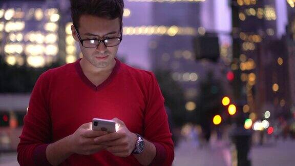 千禧一代西班牙潮男戴着眼镜一边在市中心闲逛一边在网页上打字