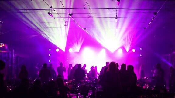 餐馆或夜总会的青年聚会餐桌上摆满了酒和食物背景是跳舞的人的剪影舞台灯光和紫色