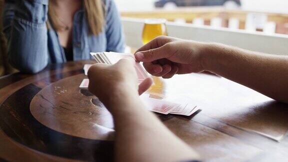 一个年轻的白人男子在一个酒吧的窗口旁边用啤酒给一个年轻的白人女子打牌