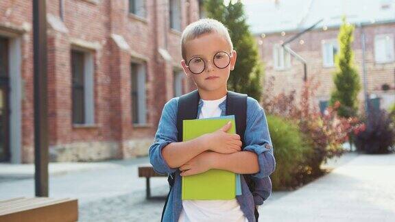 肖像小男孩拿着书站在学校附近看着相机微笑着开学前快乐的男孩站在学校门口回到学校
