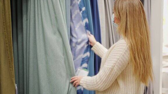 一个戴着防护面具的年轻女子在商店里选择家纺选择窗帘