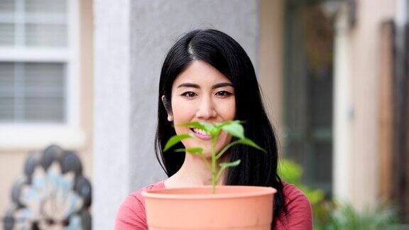 一个亚洲女人微笑着摆姿势看着镜头手里拿着一盆植物