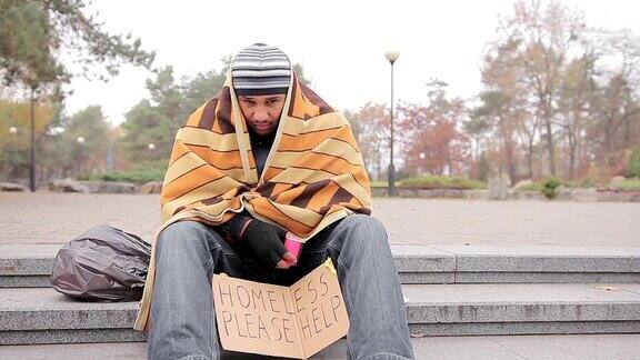 悲伤的男乞丐独自坐在公园里用旧毯子取暖男人咳嗽