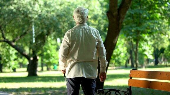 老盲人从长凳上站起来用手杖在公园里行走以清除道路