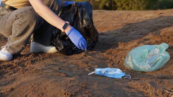 一个戴着手套的陌生女人在河岸上用黑色袋子收集垃圾戴着医用口罩慢动作