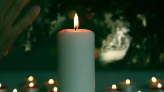 黑暗墓地的大气夜景男人的双手在墓前举着燃烧的蜡烛祈祷一支蜡烛在坟墓的背景下燃烧着秋季万圣节死者的记忆