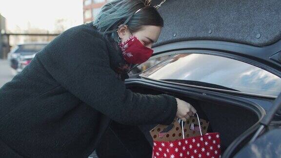 新冠肺炎疫情期间戴着防护口罩的少女在圣诞购物后将礼物放进车里
