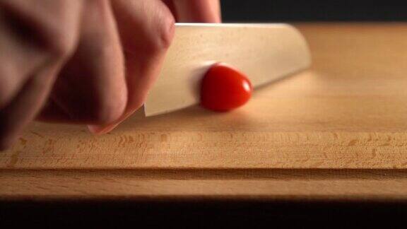 厨师将一个成熟的樱桃番茄在木板上切成两半