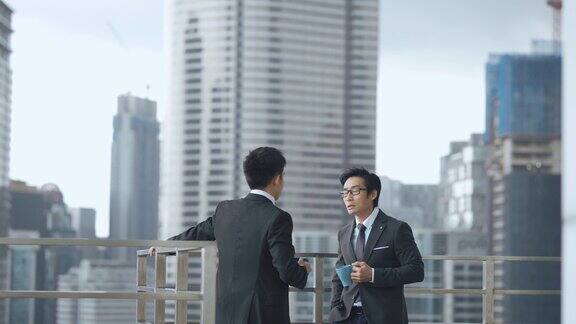 2位亚洲华人白领西装革面在办公楼阳台上休息聊天