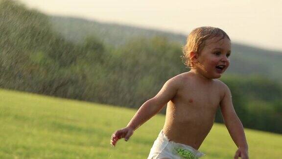 夕阳西下婴儿从洒水处跑开这是一个理想的瞬间小男孩跑出去玩了
