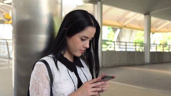 亚洲年轻的商业女性穿着白衬衫站着通过智能手机发短信