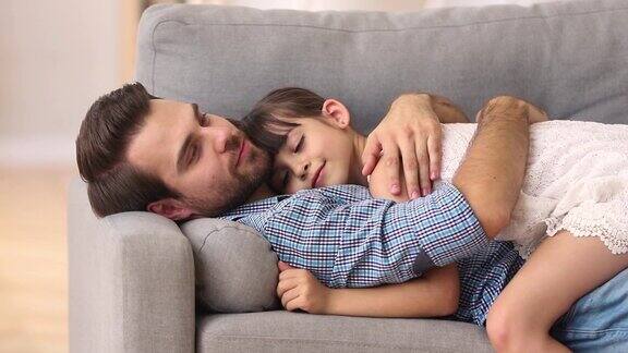 快乐的爸爸躺在沙发上抱着孩子休息依偎在一起