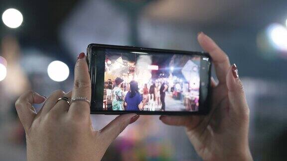 年轻的亚洲女子用手机拍了一张街头小吃市场的照片