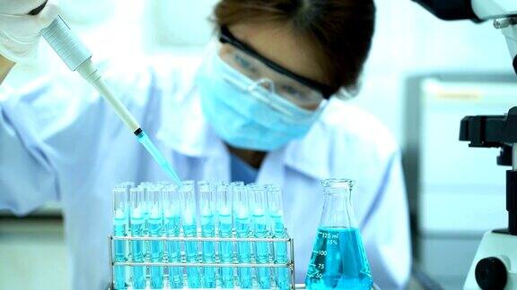 4K女科学家穿着白色防护服用吸管在实验室进行科学实验时将化学物质注入试管