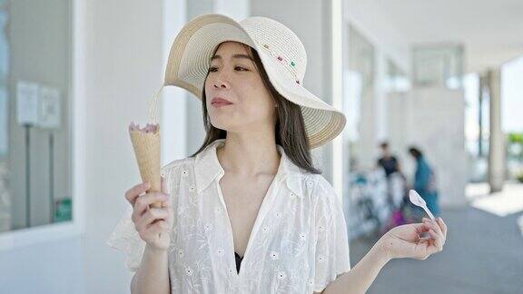 年轻的中国女游客微笑着自信地在街上吃冰淇淋