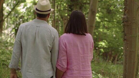跟踪镜头:一对中年夫妇在风景优美的林地里散步