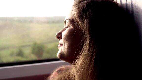 迷人的年轻女孩正对着镜头微笑乘火车旅行窗外的绿色自然女孩若有所思地看着窗外近距离
