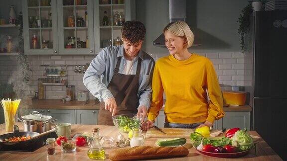 浪漫的年轻夫妇在玻璃碗里混合素食沙拉一起享受烹饪健康的食物